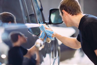 Adam parlak bir arabanın bez gövdesi ile siliyor.