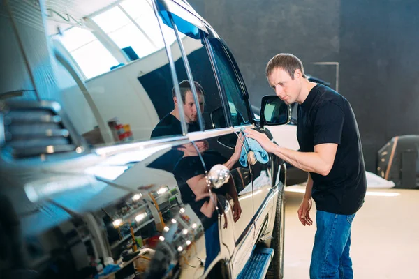 The man is wiping with a cloth body of a brilliant car.