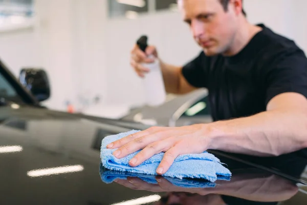 The man is wiping with a cloth body of a brilliant car.