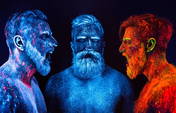 Portrait of three bearded men painted in florescent powders.