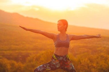 Genç kadının gün batımında veya gün doğumunda yoga ya da pilates yapan silueti, güzel bir dağ yerinde, lunge egzersizi yapıyor, Warrior ayakta.