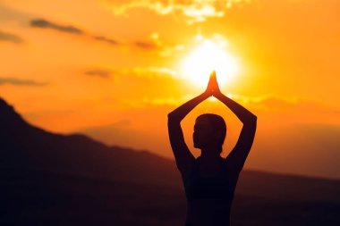 Güzel dağ yerinde gün batımında veya gün doğumunda yoga veya pilates yapan genç kadının silueti.