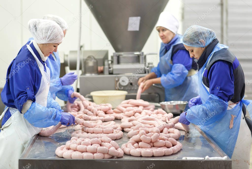 Butchers processing sausages at meat factory.