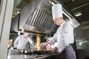 Mutfaktaki aşçı tavayla yemek pişiriyor.