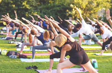 Büyük bir grup yetişkin parkta yoga dersine katılıyor..
