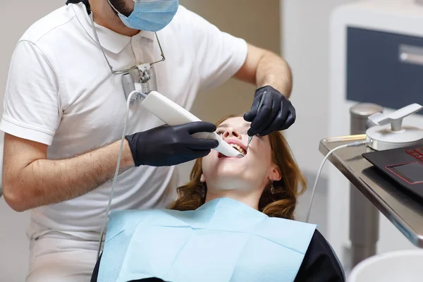 The dentist scans the patient\'s teeth with a 3d scanner.