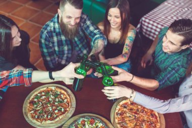 Arkadaşlar bir barda bir içki sahip, onlar bira ve pizza ile ahşap bir masada oturuyor.