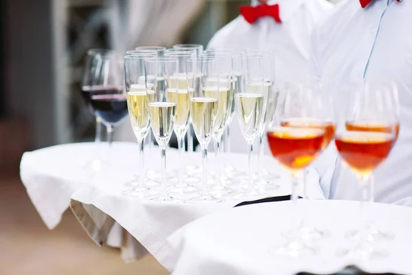 waiters greeting guests with alcoholic drinks. Champagne, red wine, white wine on trays.