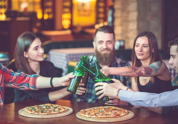 Friends having a drinks in a bar, They are sitting at a wooden table with beers and pizza.