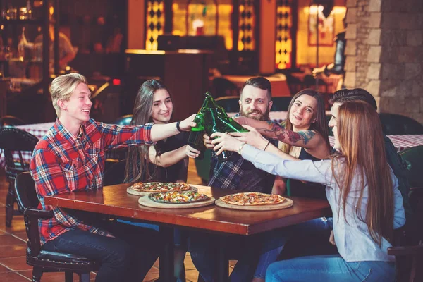 Friends having a drinks in a bar, They are sitting at a wooden table with beers and pizza.