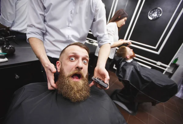 Bearded man with fear is sitting in a Barbershop.