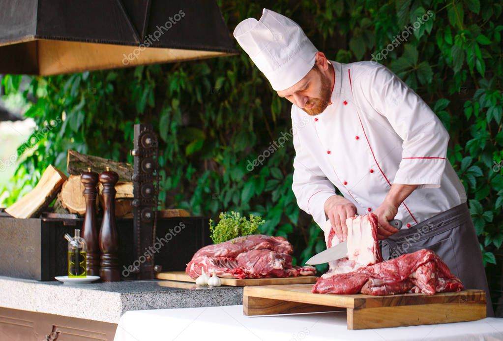 A man cook cuts meat with a knife in a restaurant.