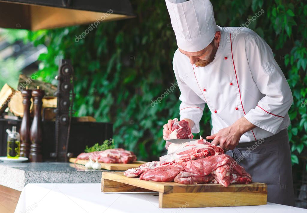 A man cook cuts meat with a knife in a restaurant.