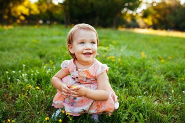 Parktaki çimlerin üzerinde oturan küçük kız.