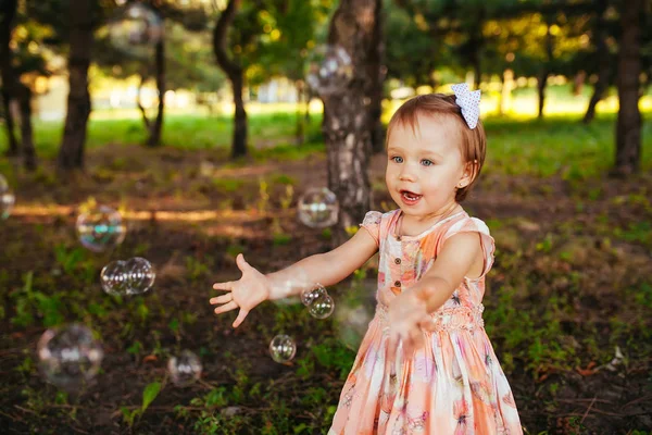 Una linda niña jugando con burbujas de jabón en el parque —  Fotos de Stock