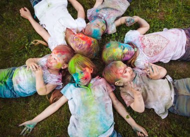 Çocuklar çimlerin üzerinde yatar. Holi festivalinin renklerine boyanmış çocuklar çimlerin üzerinde yatıyor