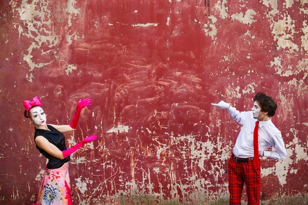Couple mimes point to center on a background of a red wall — Stock Photo, Image