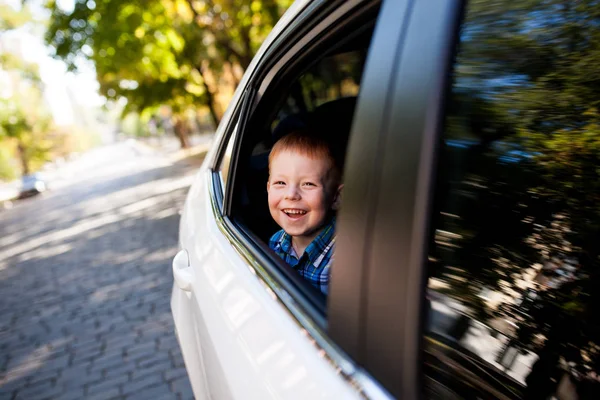 Adorable niño en el coche. Chico sonriente mira por la ventana del coche . — Foto de Stock