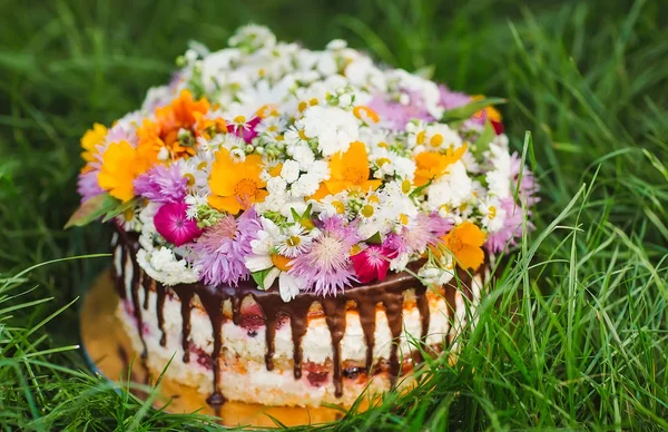 Naked cake decorated with flowers on the grass.