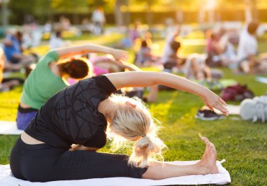 Büyük bir grup yetişkin parkta yoga dersine katılıyor.