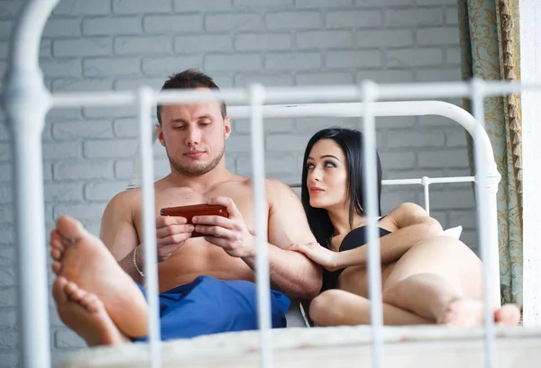 Problemas en la familia. Mujer joven enojada acostada en la cama, contra su marido, que juega el juego por teléfono . — Foto de Stock