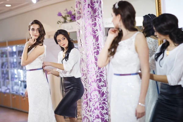 Frau probiert Hochzeitskleid im Geschäft mit weiblicher Assistentin an. — Stockfoto