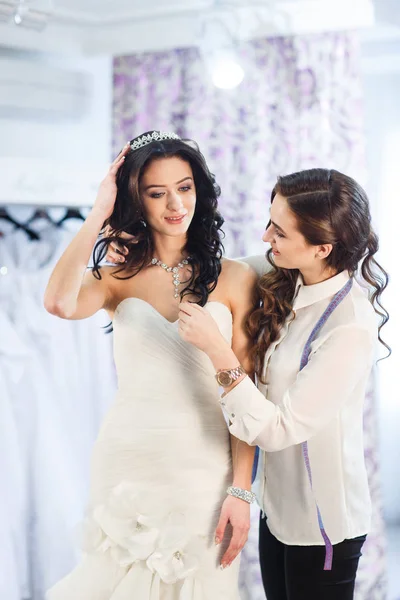 Kobieta próbuje na sukni ślubnej w sklepie z asystentem kobiet. — Zdjęcie stockowe