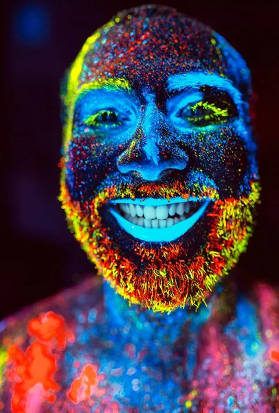 Concepto. Un hombre barbudo sonríe. Retrato de un hombre barbudo pintado en polvo fluorescente — Foto de Stock