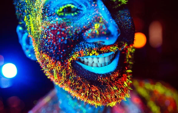 Concepto. Un hombre barbudo sonríe. Retrato de un hombre barbudo pintado en polvo fluorescente — Foto de Stock