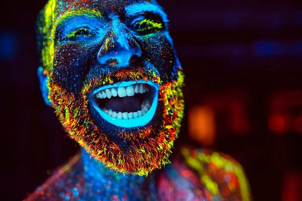Concepto. Un hombre barbudo sonríe. Retrato de un hombre barbudo pintado en polvo fluorescente . — Foto de Stock