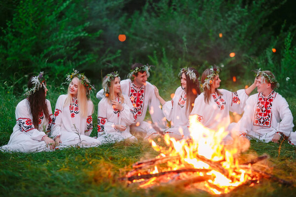 Летняя ночь. Молодые люди в славянской одежде сидят у костра
