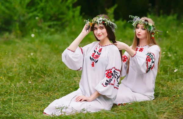 Hochsommer. zwei Mädchen in slawischer Kleidung flechten Zöpfe in die Haare am Feuer — Stockfoto