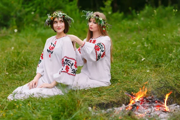 No meio do verão. Duas meninas nas roupas eslavas tecem tranças no cabelo perto do fogo — Fotografia de Stock
