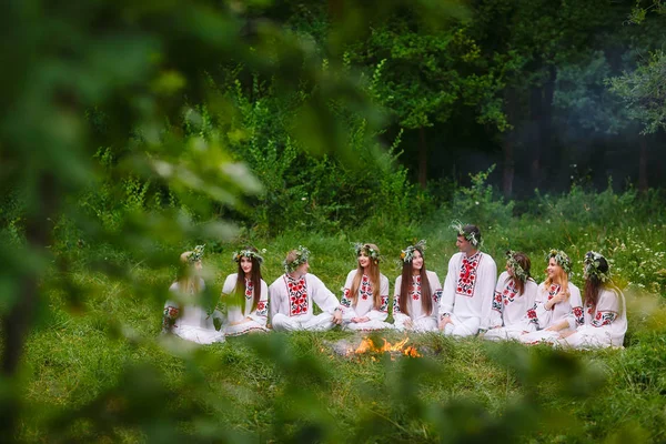 Hochsommer. Junge Leute in slawischer Kleidung sitzen im Wald am Feuer. — Stockfoto
