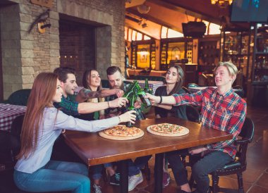 Arkadaşlar bir barda bir içki sahip, onlar bira ve pizza ile ahşap bir masada oturuyor.