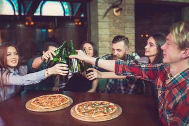 Arkadaşlar bir barda bir içki sahip, onlar bira ve pizza ile ahşap bir masada oturuyor