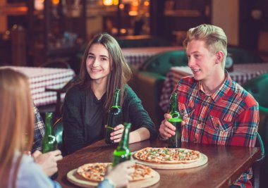 Arkadaşlar bir barda bir içki sahip, onlar bira ve pizza ile ahşap bir masada oturuyor