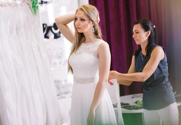 Frau probiert Hochzeitskleid im Geschäft mit weiblicher Assistentin an. — Stockfoto