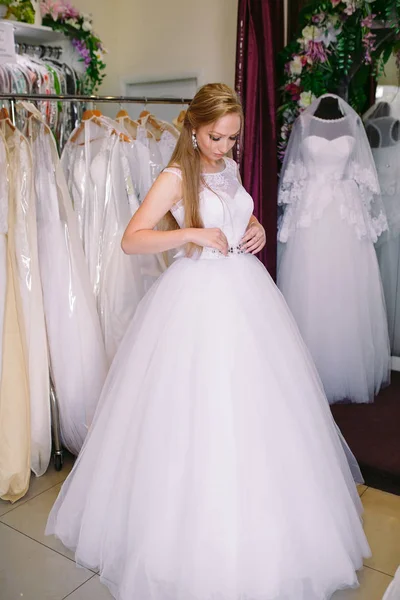 Žena se snaží na svatební šaty v obchodě s ženy asistent. — Stock fotografie