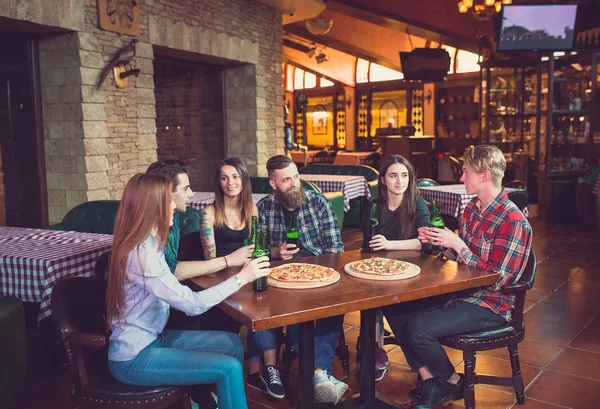 Amigos tomando una copa en un bar, están sentados en una mesa de madera con cervezas y pizza —  Fotos de Stock