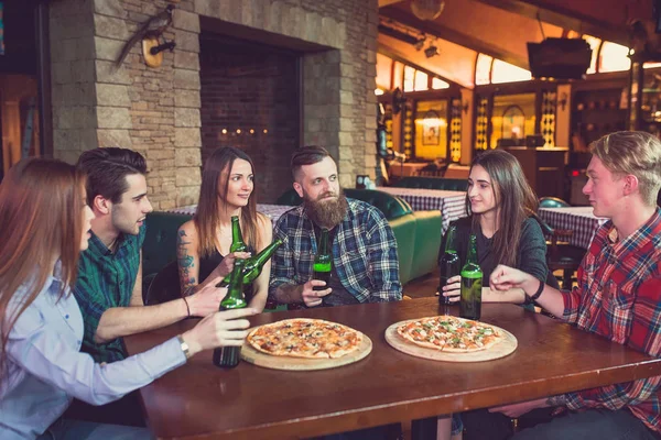 Amigos tomando una copa en un bar, están sentados en una mesa de madera con cervezas y pizza . —  Fotos de Stock