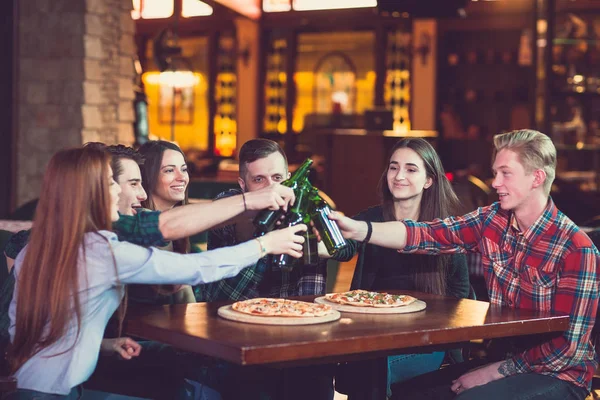 Arkadaşlar bir barda bir içki sahip, onlar bira ve pizza ile ahşap bir masada oturuyor