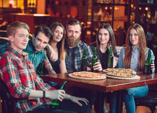 Amigos tomando una copa en un bar, están sentados en una mesa de madera con cervezas y pizza —  Fotos de Stock