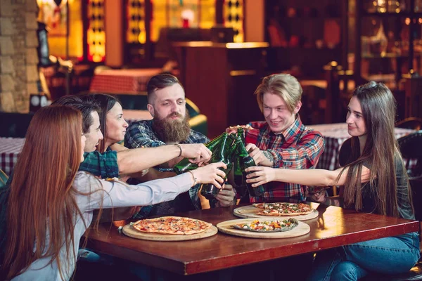 Amigos tomando una copa en un bar, están sentados en una mesa de madera con cervezas y pizza —  Fotos de Stock
