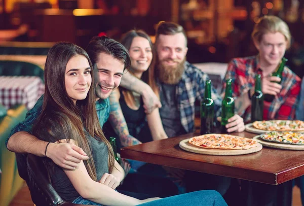 Amigos tomando una copa en un bar, están sentados en una mesa de madera con cervezas y pizza —  Fotos de Stock