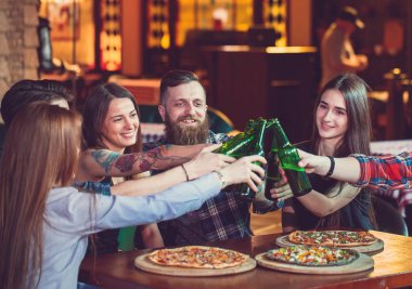 Arkadaşlar bir barda bir içki sahip, onlar bira ve pizza ile ahşap bir masada oturuyor.