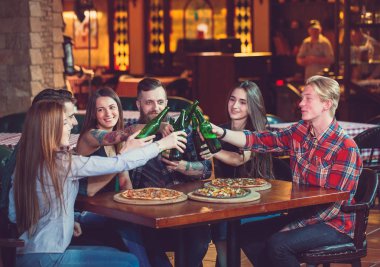 Arkadaşlar bir barda bir içki sahip, onlar bira ve pizza ile ahşap bir masada oturuyor.