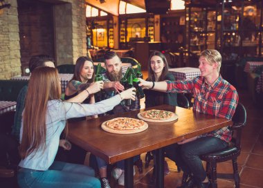 Arkadaşlar bir barda bir içki sahip, onlar bira ve pizza ile ahşap bir masada oturuyor