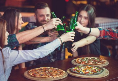 Arkadaşlar bir barda bir içki sahip, onlar bira ve pizza ile ahşap bir masada oturuyor.