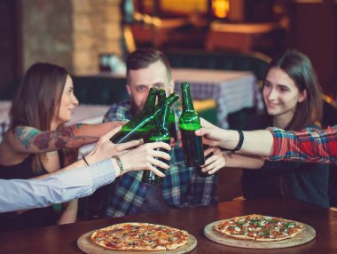 Arkadaşlar bir barda bir içki sahip, onlar bira ve pizza ile ahşap bir masada oturuyor.